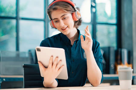 Video Conference. Portrait of cheerful woman in headset having web call using tablet, She talking waving hand at webcam in home office.の写真素材