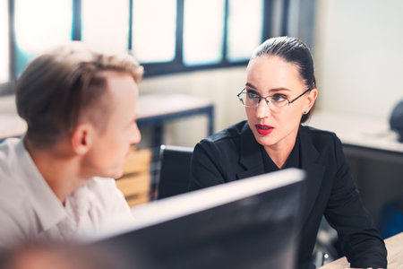 Two diverse business people chatting sitting front laptop in office. Male sharing ideas or startup business plan with female coworker. Business planning.の写真素材