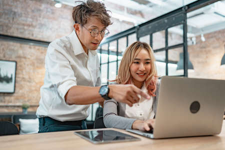 Two asian business people chatting sitting front laptop in cafe. Male sharing ideas or startup business plan with female coworker. Business planning.の写真素材