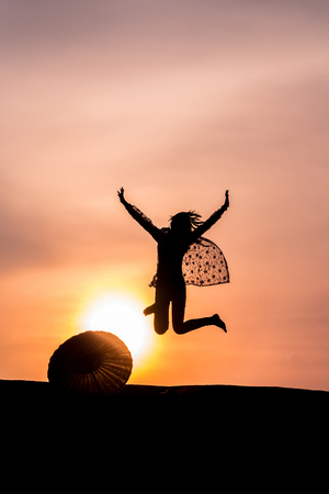 silhouette of women happy jumping against sunset.の写真素材