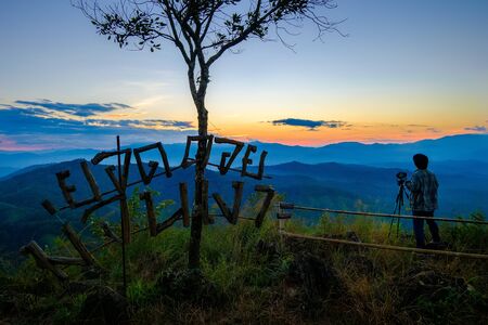 Silhouette of male photographer or traveler taking a photograph of sunrise landscape on mountain top