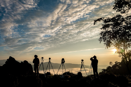 Silhouette of male photographer or traveler taking a photograph of sunrise landscape on mountain top