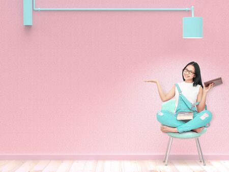 Young Woman students sit on a chair under the lamp and pink wall background. pastel color and present idea concept.の写真素材