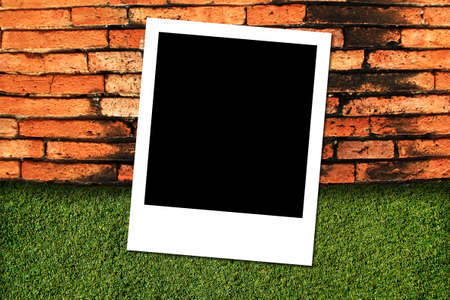 Photo frame on green grass and brick wall background の写真素材