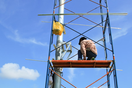 Construction workers on scaffold working under a blue sky.のeditorial素材