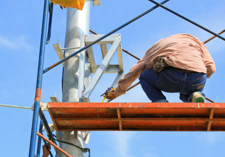 Construction workers on scaffold working under a blue sky.