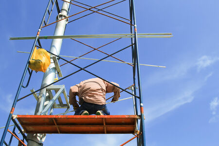 Construction workers on scaffold working under a blue sky.の写真素材