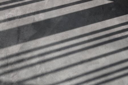 Empty floor and diagonal shadows on gray wall.