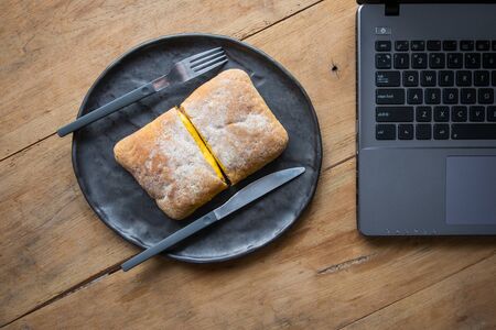 Laptop on wooden table with breakfast during rush hour time. Time management concept.の写真素材