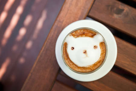 Coffee topping bear made with milk foam. Cup of hot coffee place on the wood table.の写真素材