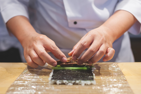 Cook hands making japanese sushi roll. Japanese chef preparing sushi roll with rice on nori leaf.の写真素材