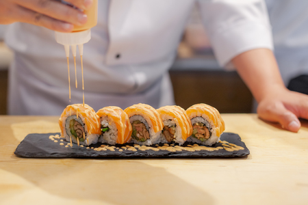 Hands chef preparing japanese sushi, pouring sauce on salmon roll.の写真素材