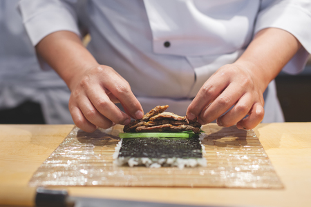 Cook hands making japanese sushi roll. Japanese chef preparing sushi roll with rice on nori leaf.の写真素材