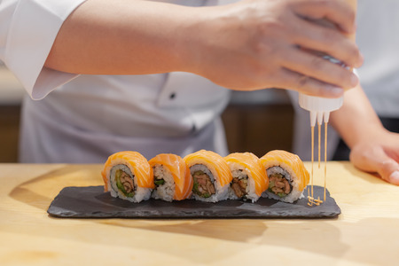 Hands chef preparing japanese sushi, pouring sauce on salmon roll.の写真素材