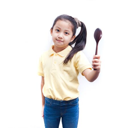 Asian little girl kid wearing a yellow shirt, and holding fwooden spoon on white background.の写真素材