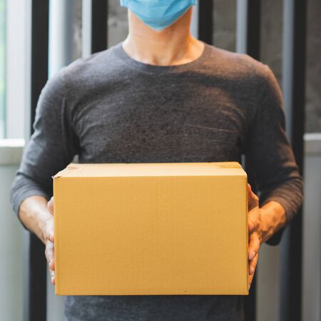 Delivery man wearing protective face mask.
Courier delivering cardboard box in surgical gloves and surgical mask.の写真素材