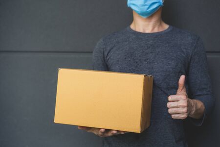Delivery man wearing protective face mask.
Courier delivering cardboard box in surgical gloves and surgical mask.の写真素材