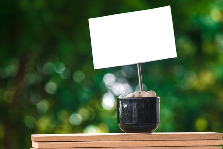 paper of note on a coffee cup with stone on a wooden board and a Bokeh tree backdrop.
