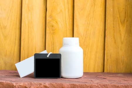 Bottle made to plastic and notepad on the wood with wall background. Using wallpaper for package or...