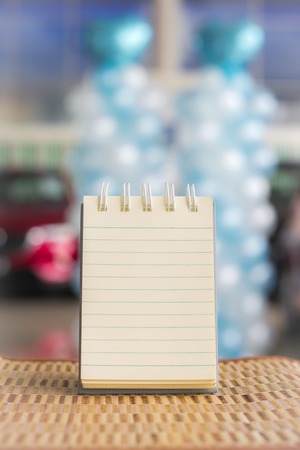 Notepad with wine glass on wood board background.  Blurry in showroom car background. using...