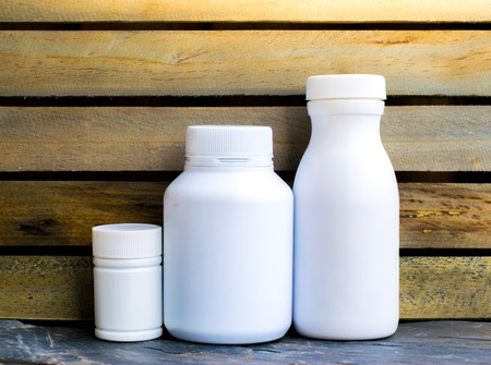 Bottle made to plastic and notepad on the wood with wall background. Using wallpaper for package or product and drug image.の写真素材