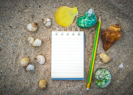 Notepad with pencil and starfish, shellfish on sand background or on the beach of sea using wallpaper for education, business photo. Take note of the product for book with paper concept or copy space and refreshing.の写真素材