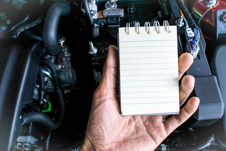 man holding notepad engine of car on blurry foreground with background. Wait maintenance for note customer information, transportation with car part and fix car insurance image.の写真素材