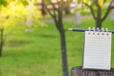 Notepad with pencil on wood board and tree blurry background. using wallpaper or background for education, business photo. Take note of the product for book with paper and concept or copy space and note.の写真素材