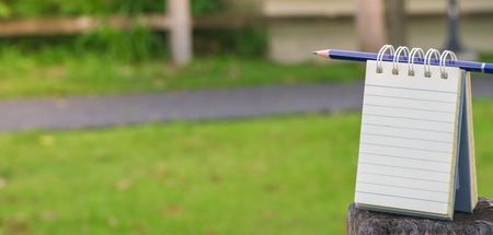 Notepad with pencil on wood board and tree blurry background. using wallpaper or background for education, business photo. Take note of the product for book with paper and concept or copy space and note.の写真素材
