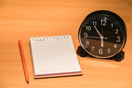 Notepad with clock on wood board background. using wallpaper or background for education, business photo. Take note of the product for book with paper and concept or copy space and note.の写真素材