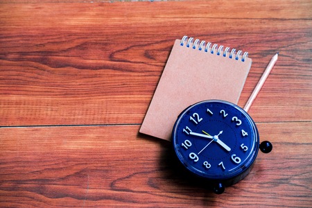 Notepad with clock on wood board tree blurry background. using wallpaper or background for education, business photo. Take note of the product for book with paper and concept or copy space and note.の写真素材