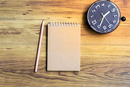 Notepad with clock on wood board tree blurry background. using wallpaper or background for education, business photo. Take note of the product for book with paper and concept or copy space and note.の写真素材