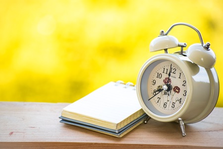 Notepad with clock on wood board tree blurry background. using wallpaper or background for...