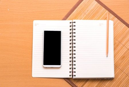 notepad with smart phone on wood board background.using wallpaper for education, business photo.Take note of the product for book with paper and concept or copy space.の写真素材