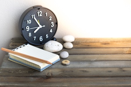 Notepad with pencil and clock on wood board background.using wallpaper for education, business...