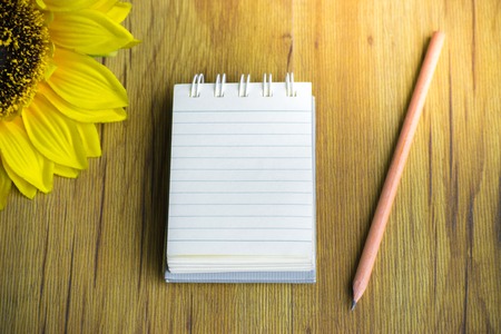 Notepad with pencil and sunflower on wood board background.using wallpaper for education, business photo.Take note of the product for book with paper and concept or copy space.の写真素材