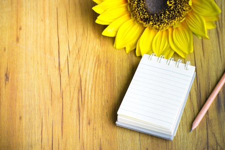 Notepad with pencil and sunflower on wood board background.using wallpaper for education, business photo.Take note of the product for book with paper and concept or copy space.の写真素材