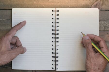 man writing on notepad or book, paper on wood background. Using wallpaper or background for note...