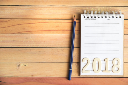 Notepad with pencil and number 2018 on wood board background.using wallpaper for education, business...
