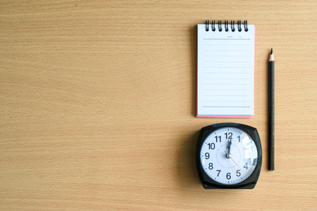 Notepad with pencil and clock on wood board background.using wallpaper for education, business photo.Take note of the product for book with paper and object, concept or copy space.の写真素材