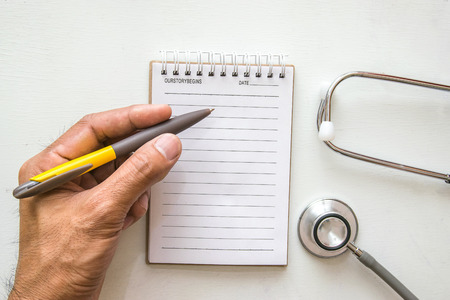 Man writing Notebook, pen and Medical Headphones stethoscope on table. For medical notes imageの写真素材