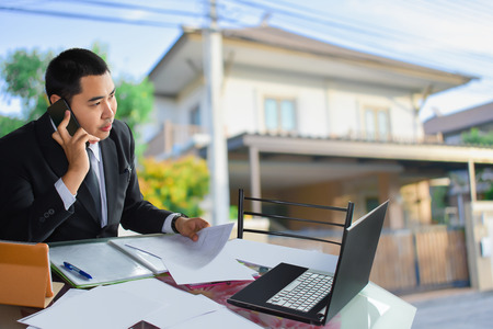 Man business salesman Sell house with computer On house and tree blurry background.For home business contracting or agreement and home warranty image.の写真素材