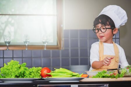 Asian Boy son cooking salad food holdind wooden spoon with vegetable holding tomatoes and carrots, bell peppers on plate for happy family cook food enjoyment lifestyle kitchen in homeの写真素材