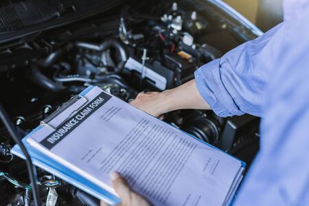 Asian Man mechanic inspection writing note on clipboard.Blue car for service maintenance insurance with car engine.for transport automobile automotive image.の写真素材