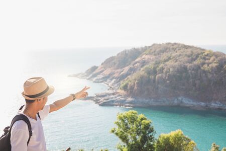 Man wearing hat holds his hand happy. Man asian tourist Look at mountains and the sea Before sunset.for activity lifestyle outdoors freedom or travel tourism inspiration backpacker tourist to covid 19の写真素材