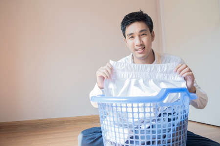 Asian man husband working homework.He is preparing clothes in basket to wash to washing machine for service lifestyle family togetherness in homeの写真素材