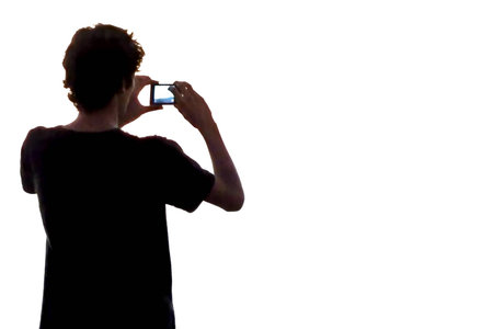 Teenage boy taking a picture with his cellphone on a white background.の写真素材