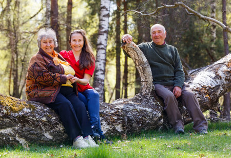 Elderly couple and young caregiver sitting on tree trunk in the parkの写真素材