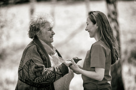 Elderly woman and young caregiver walking in the park