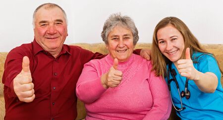 Happy elderly couple and young caregiver showing thumbs up